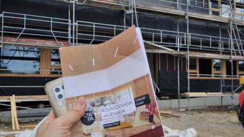 Une personne tenant un document devant un bâtiment lors de la visite de chantier à Rountzenheim-Auenheim.