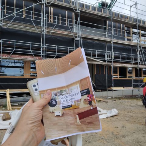 Une personne tenant un document devant un bâtiment lors de la visite de chantier à Rountzenheim-Auenheim.