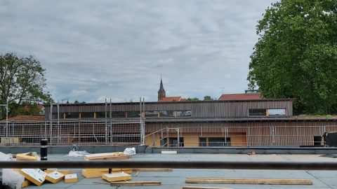 Toit en métal avec un bâtiment en arrière-plan, lors de la visite de chantier du groupe scolaire à Rountzenheim-Auenheim.