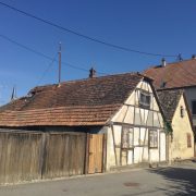 Petite maison alsacienne avec toit rouge et clôture en bois, avant son démontage.